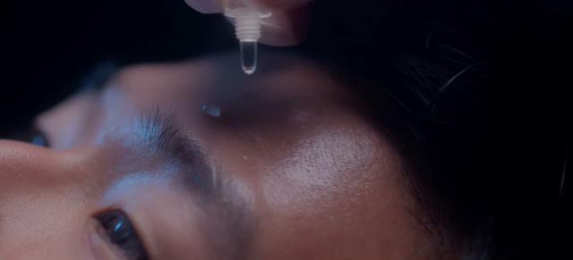 Close up of a face in profile with a dropper releasing a drop above the eye. Frame from the commercial Saelo, Skin treatments.