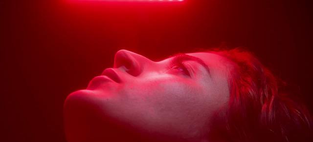 A person lies on their back in profile, lit in deep red light from above, eyes closed. Frame from the commercial Saelo, Skin treatments.